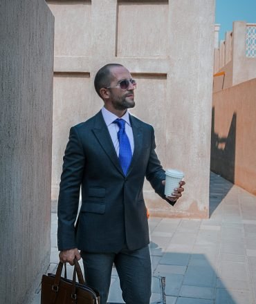 Professional businessman in a suit, holding coffee, walking outdoors in Dubai.