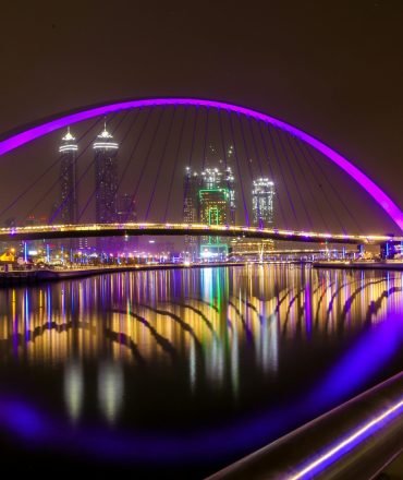 Stunning nighttime view of the illuminated Tolerance Bridge over the Dubai Canal in UAE, showcasing vibrant reflections.