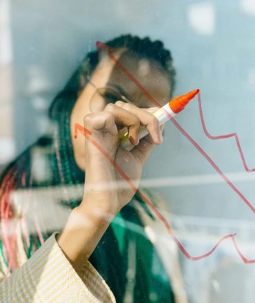 A businesswoman draws a red financial graph on a glass panel, symbolizing strategy and success.